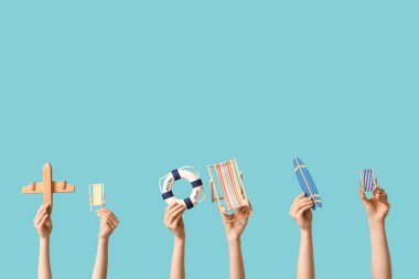 Mavi arka planda sörf tahtası, uçak ve can simidi olan mini güverte sandalyeleri tutan kadın eller.