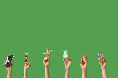 Yeşil zemin üzerinde güneş gözlüğü, kamera ve deniz yıldızı olan mini güverte sandalyeleri tutan kadın eller.