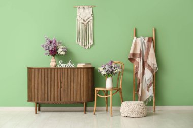 Sandalyeli, tuvaletli ve vazolarında leylak çiçekleri olan oturma odasının içinde.