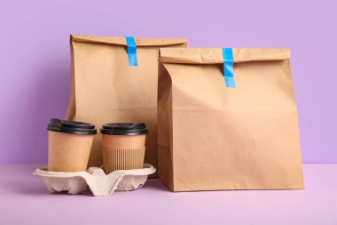 Leylak arkaplanda kahve fincanları olan kağıt torbalar. Yemek dağıtım servisi.