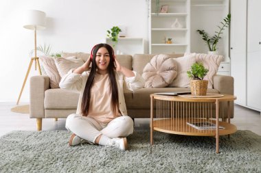 Kulaklıklı genç bir kadın evde müzik dinliyor.