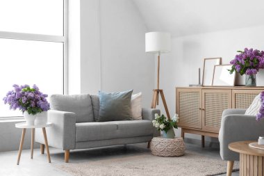 Kanepe ve vazolarda leylak çiçekleriyle aydınlık oturma odasının içinde.