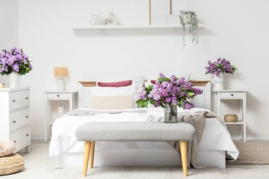 Hafif yatak odasının içinde, yumuşak bir bank ve vazolarda leylak çiçekleri.
