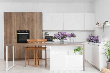 Masa, tezgah ve vazolarda leylak çiçekleri olan açık mutfak.