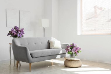 Kanepe, lamba ve vazodaki leylak çiçekleriyle aydınlık oturma odasının içinde.