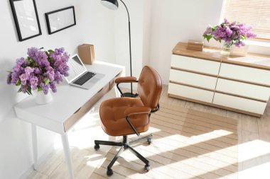 İş yeri, lamba ve vazoda leylak çiçekleri olan ışık ofisinin içinde.