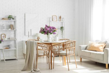 İçinde yemek masası, kanepe ve vazoda leylak çiçekleri olan bir oda.