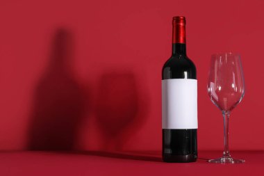 Boş etiketli bir şişe şarap ve kırmızı arka planda boş bardak.
