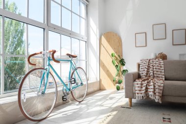 Oturma odasının içinde bisiklet, pencere ve kanepe var.