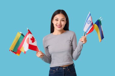 Mavi arka planda farklı ülkelerin bayrakları olan genç bir Asyalı kız.