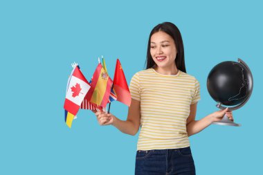 Farklı ülkelerden bayrakları ve mavi arka planda küresi olan Asyalı genç bir kız.