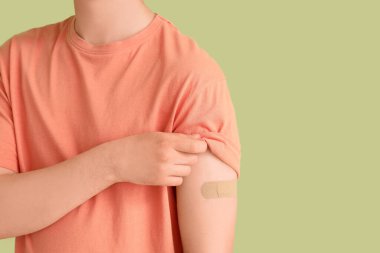 Yeşil arka planda uygulamalı tıbbi yaması olan genç bir adam, yakın plan. Aşılama kavramı