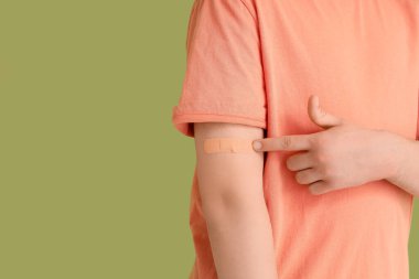 Yeşil arka planda uygulamalı tıbbi yamaya işaret eden genç adam, yakın plan. Aşılama kavramı