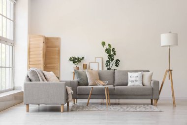 Gri kanepeler, lamba ve katlanan ekran ile aydınlık oturma odasının içi