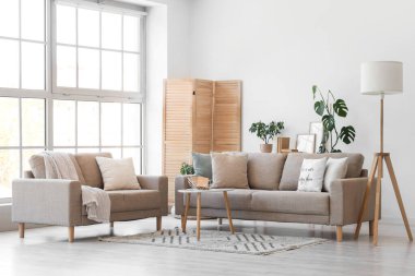 Gri kanepeler, lamba ve katlanan ekran ile aydınlık oturma odasının içi