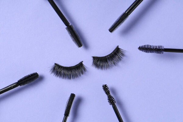 Black mascara brushes and false eyelashes on purple background