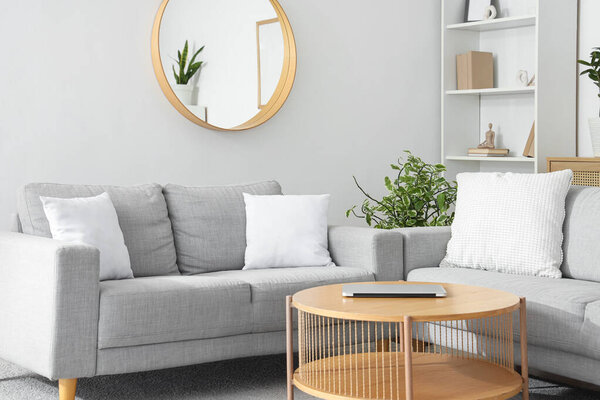 Interior of light living room with grey sofas, table and mirror