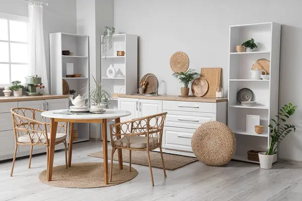 Mutfağın içinde raf üniteleri, tezgahlar ve yemek masası var.