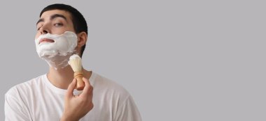 Gri arkaplan üzerinde tıraş olan genç adam mesaj için yer açıyor