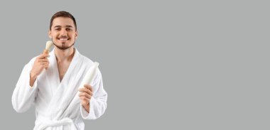 Tıraş fırçası ve köpüğü olan yakışıklı genç bir adam. Arka planı gri ve metin için yeri var.