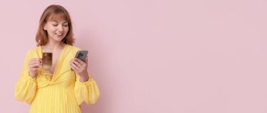 Bir bardak lezzetli buzlu latte ve pembe arka planda cep telefonu olan mutlu genç bir kadın.