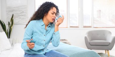 Yatak odasında astım spreyi kullanan Afro-Amerikalı genç bir kadın.