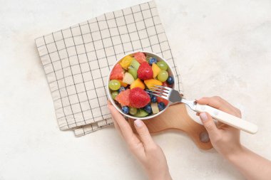 Kadın arka planda taze meyve salatası yiyor.