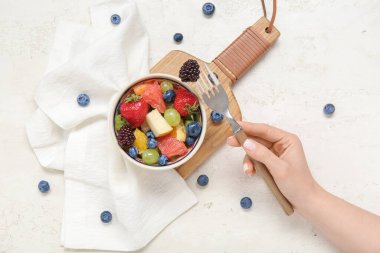 Kadın arka planda taze meyve salatası yiyor.