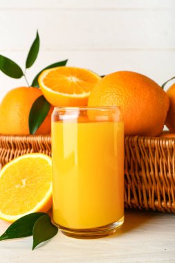 Bir bardak taze portakal suyu ve beyaz arka planda meyveli hasır sepet.