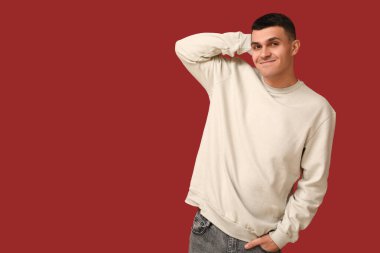 Kırmızı arka plandaki yakışıklı, utangaç genç adam.