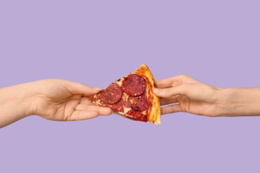 Kadın eli, leylak arkaplanda lezzetli bir pizza dilimi veriyor.