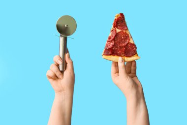 Lezzetli pizza dilimleri ve mavi arka planda pizza kesicisi tutan kadın eller.