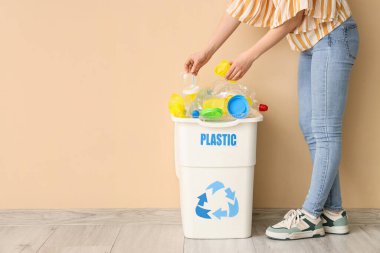 Bej duvarın yanında plastikçilik işareti olan çöp kutusuna çöp atan bir kadın. Geri dönüşüm kavramı