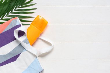 Beyaz ahşap arka planda kozmetik çanta, güneş kremi ve palmiye yaprağı ile güzel bir kompozisyon