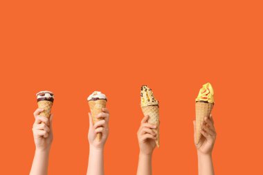 Turuncu arka planda waffle külahlı farklı tatlı dondurmalı kadın elleri.