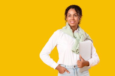 Sarı arka planda dizüstü bilgisayarı olan genç bir Afro-Amerikan soru cevap mühendisi.