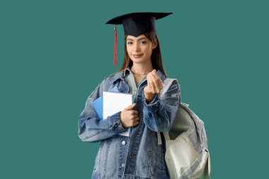 Mezuniyet şapkalı, yeşil arka planda defterleri olan bir kız öğrenci. Eğitim tasarruf kavramı