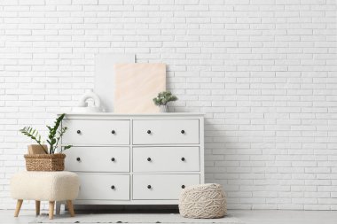 Çekmeceler, puflar, ev bitkileri ve odanın beyaz tuğla duvarının yanındaki çerçeveler.