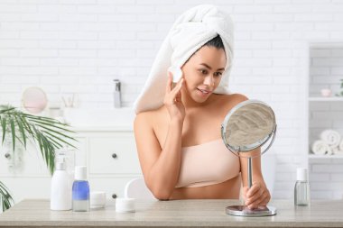 Güzel bir Afro-Amerikalı kadın. Banyoda bir şişe mikiler suyu ve pamuk pedi var.