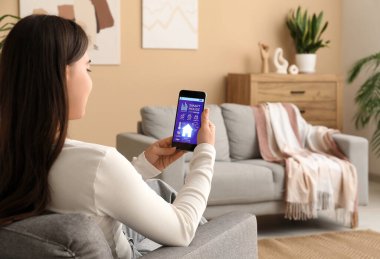 Akıllı ev güvenlik sistemi uygulaması kullanan cep telefonu olan genç bir kadın.