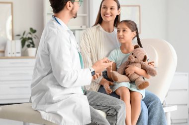 Oyuncak ayıyla tatlı bir kız ve annesi klinikteki çocuk doktorunu ziyaret ediyor.