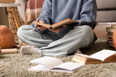 Evde halıda kitap okuyan bir kadın.