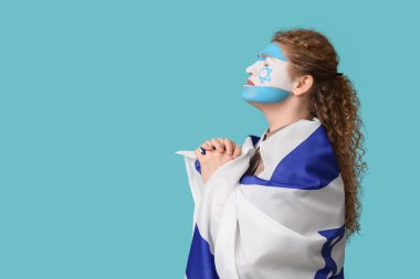 Yüzü boyalı genç bir kadın ve mavi arka planda dua eden İsrail bayrağı. Uluslararası Soykırım Anma Günü