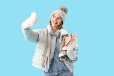 Kışın buz pateni giymiş genç bir kadın mavi arka planda selfie çekiyor.