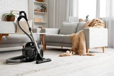 Oturma odasının içinde elektrikli süpürge, kanepe ve masa var.