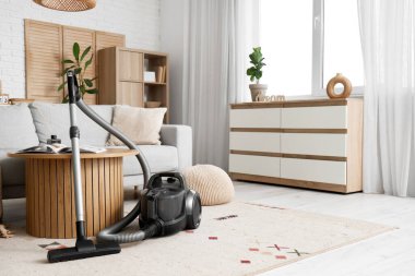 Oturma odasında elektrikli süpürge, masa ve kanepe var.