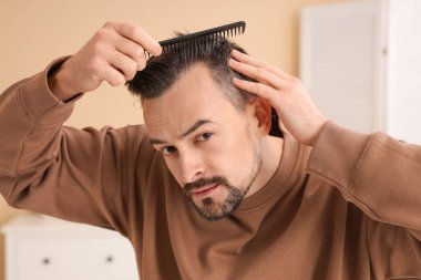 Saç dökülme sorunu olan yakışıklı adam banyoda tarama yapıyor, yakın plan.