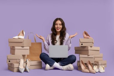 Laptop ve ayakkabı kutularıyla genç Asyalı kadın leylak arka planda alışveriş yapıyor.