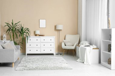 Aydınlık oturma odasının içinde çekmeceler, kanepe ve bej duvarın yanındaki koltuk.