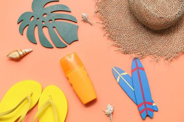 Parmak arası terlikli mini sörf tahtaları, güneş kremi ve turuncu arka planda hasır şapka. Yaz konsepti